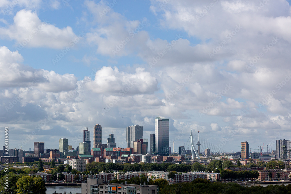 Downtown cityscape of the modern city of Rotterdam with high rise buildings, a neighbourhood, a river passing and dramatic clouds in the blue sky