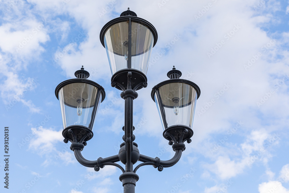 Close-up of three black street lamps on one column against blue sky