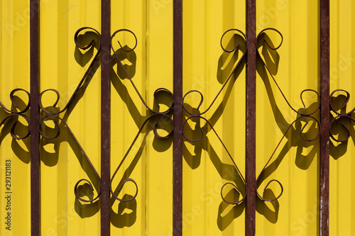 Close-up of wrought iron fence against yellow wall