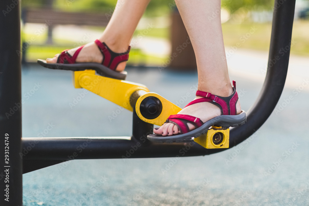 Urban environment: outdoor fitness equipment, legs of a girl on a public outdoor exercise bike Urban environment: outdoor fitness equipment, legs of a girl on a public outdoor exercise bike