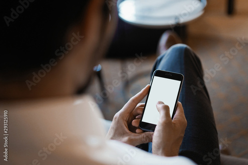 Smiling bearded man making text message on smartphone while sitting sofa at modern office.