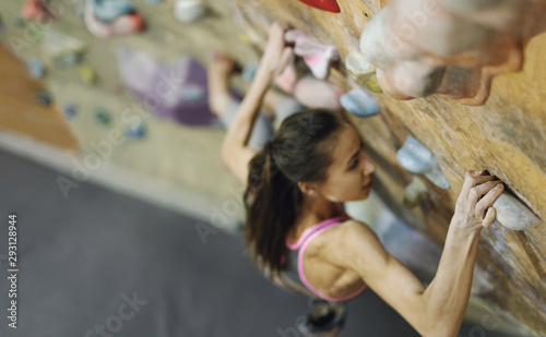 Young Woman Rock climber is Climbing At Inside climbing Gym. slim pretty Woman Exercising At Indoor Climbing Gym Wall