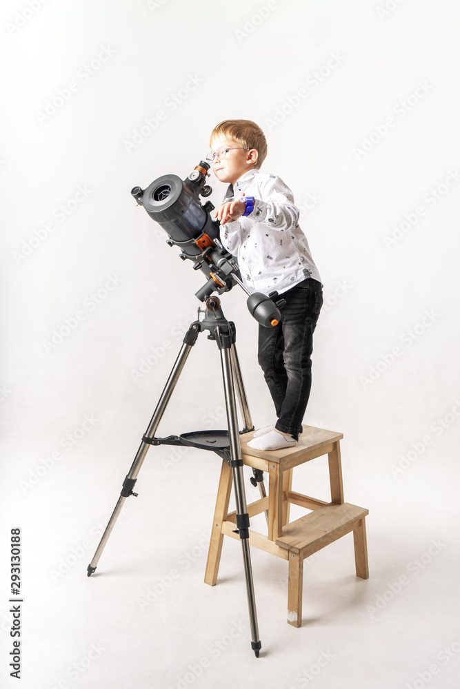 A little boy with glasses looks through a large reflex telescope.