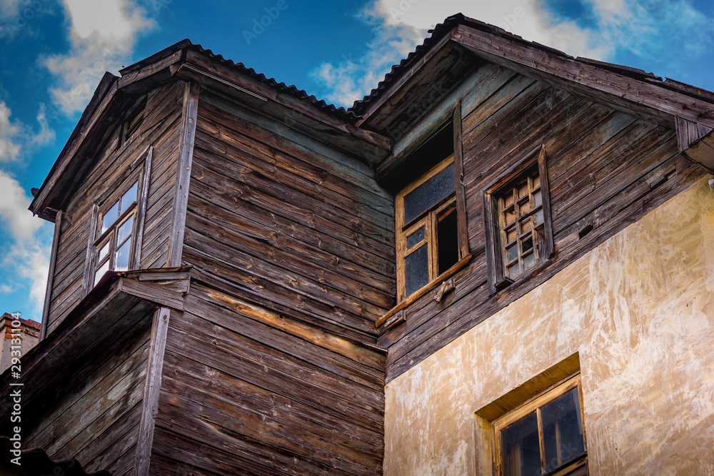 old village house of concrete and wood with windows. bottom view on the background of blue sky in the clouds. old village house of concrete and wood with windows. bottom view on the background of blue sky in the clouds.