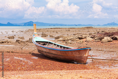 Traditional Thai longtail boat on the sand beach at the low tide. Sea view with islands on horizon and clouds in the sky.