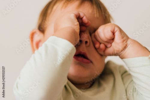 Fotografía Sleepy baby rub her eyes. CLose up portrait of tired toddler
