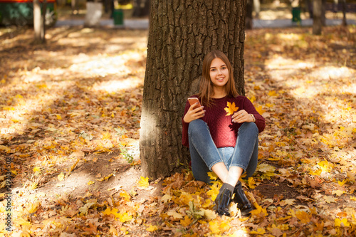 Young woman in a sweater and blue jeans sits in an autumn park