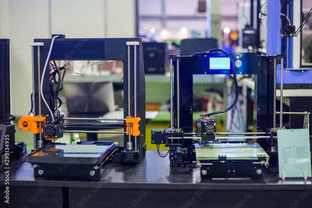 Two automatic 3D printers during work at modern technology exhibition. 3D printing, additive technologies, 4.0 industrial revolution and futuristic concept Two automatic 3D printers during work at modern technology exhibition. 3D printing, additive technologies, 4.0 industrial revolution and futuristic concept