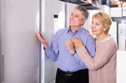 mature married couple in shop of household appliances are choosing home modern refrigerator
