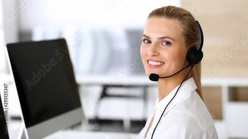 Call center. Happy and excited business woman using headset while consulting clients online. Customer service office or telemarketing department. Smiling blonde female operator at work