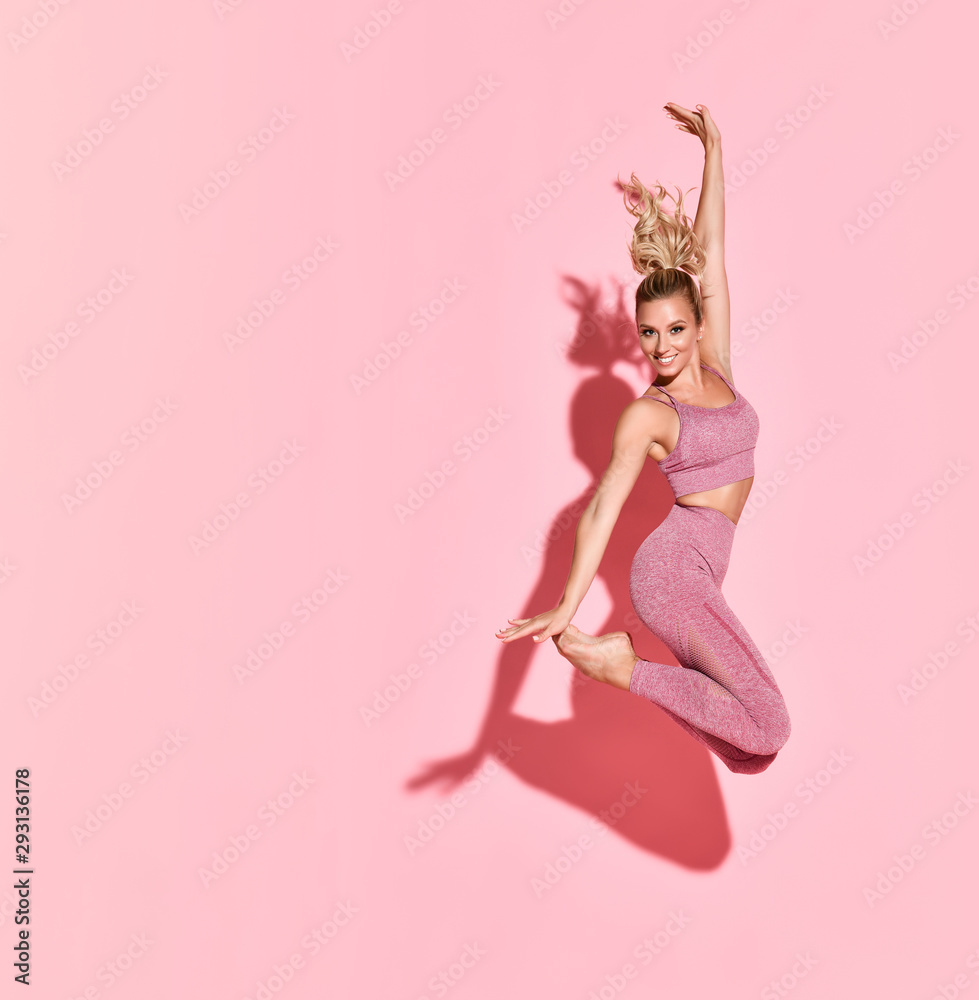 Fototapeta premium Szczęśliwa kobieta lekkoatletycznego skoki w sylwetce. Zdjęcie sportowej kobiety w modnej różowej odzieży sportowej na różowo