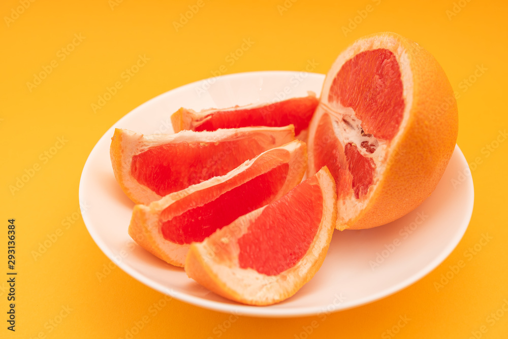 Fresh ripe juicy grapefruit on white plate on yellow background.