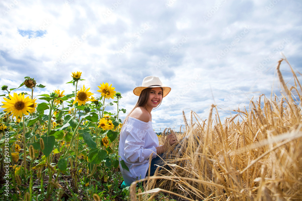 Brunette woman in white blouse sitting on a background of golden wheat and sunflowers fields Brunette woman in white blouse sitting on a background of golden wheat and sunflowers fields