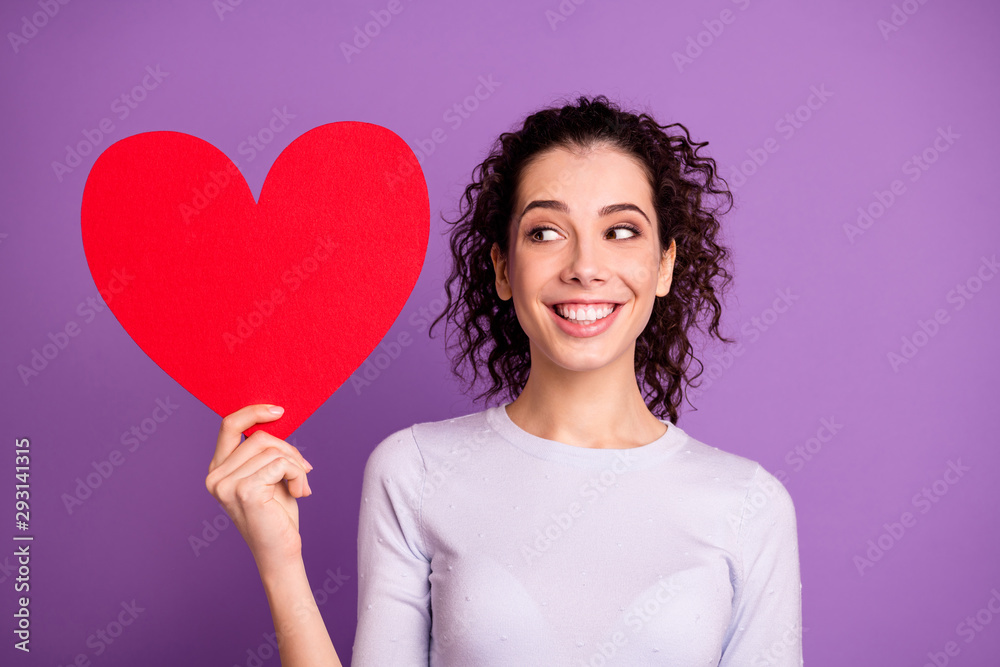 Photo of cheerful wavy nice charming sweet girlfriend smiling toothily holding red shape heart guessing who she received it from isolated over violet pastel color background Photo of cheerful wavy nice charming sweet girlfriend smiling toothily holding red shape heart guessing who she received it from isolated over violet pastel color background