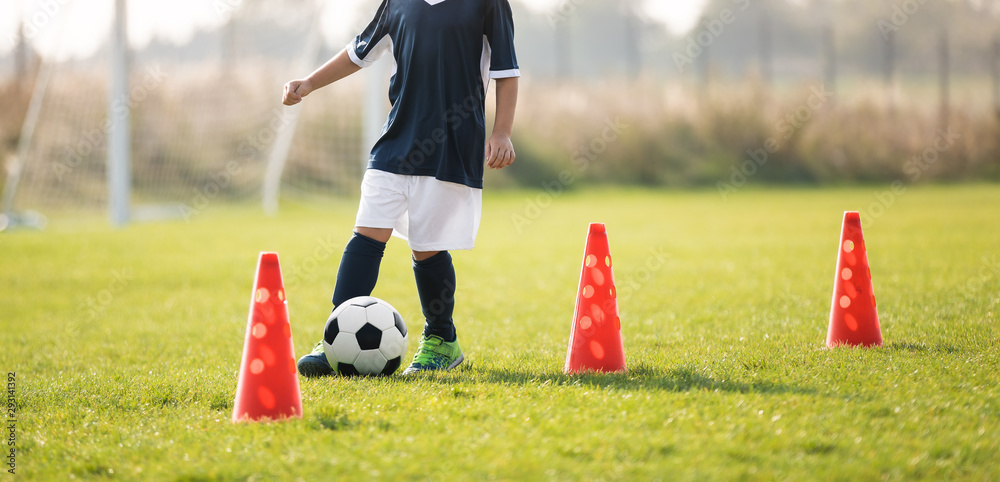 Obraz premium Soccer player dribbling through cones in the ground on a sunny. Young boy soccer (european football) player dribble through cones