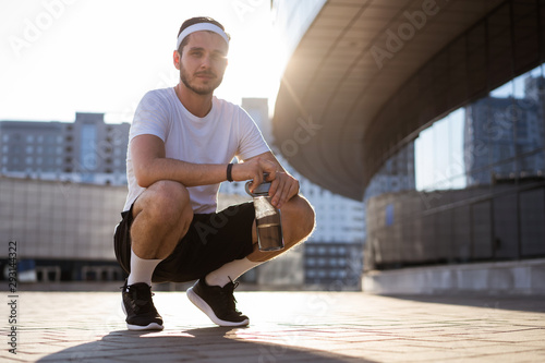 Young athlete in windrunner sitting on the street after good jogging session at sunset. photo