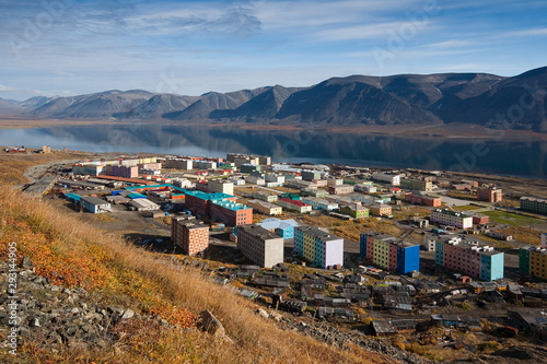 Top view of the small arctic port town of Egvekinot. Colorful buildings on the shore among the mountains. Location place: Kresta Bay of Bering sea, Egvekinot, Chukotka, Siberia, Far East of Russia.