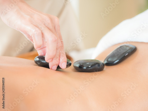An expert masseuse at a spa salon puts hot stone on the back of an Asian woman to relieve tension from work