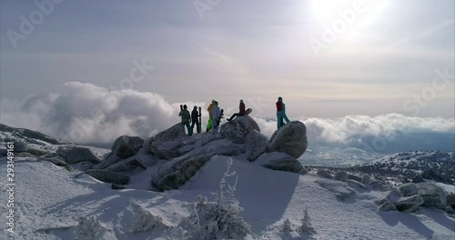 4K aerial winter peak. a group of skiers and snowboarders on top of a mountain. epic dawn of the sun in winter at the top with a group of freeriders. beautiful snow blows and glitter of snowflakes.