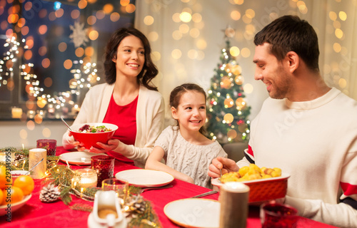 holidays, family and celebration concept - happy mother, father and little daughter having christmas dinner at home