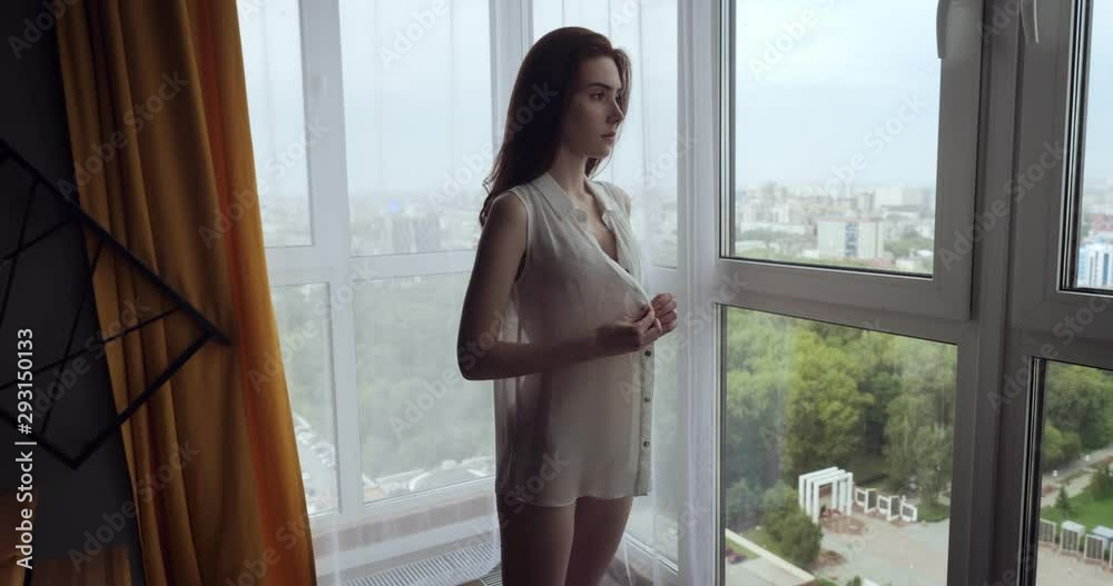 Redhead woman fustens the buttons of white blouse at home.