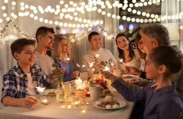 celebration, holidays and christmas concept - happy family with sparklers having fun at dinner party at home