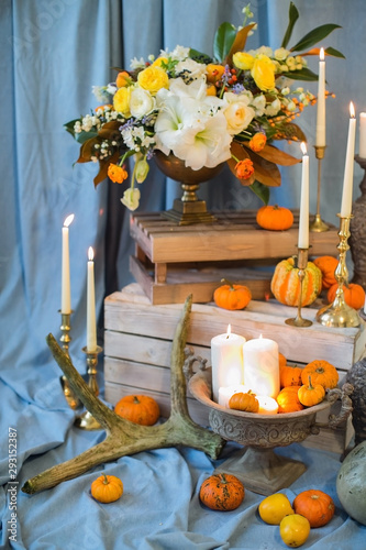 Bronze vase in which stands a bouquet of lily flowers, a peony rose, eustoma and green leaves with persimmons and red berries. Flowerpot on a white box, orange pumpkins, autumn mood. Luxury Wedding.