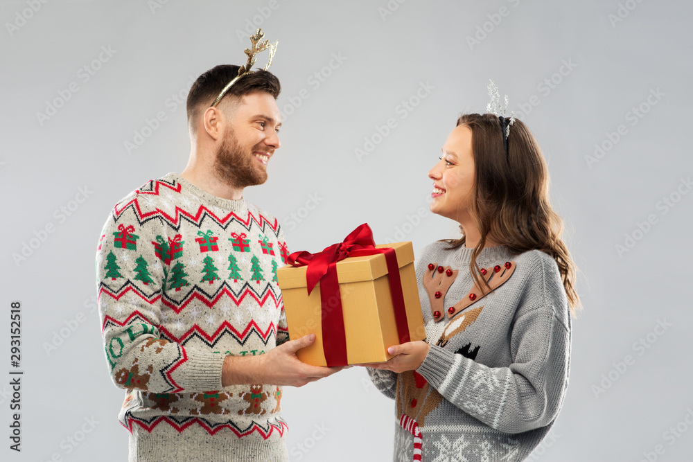 people and holidays concept - portrait of happy couple with christmas gift at ugly sweater party