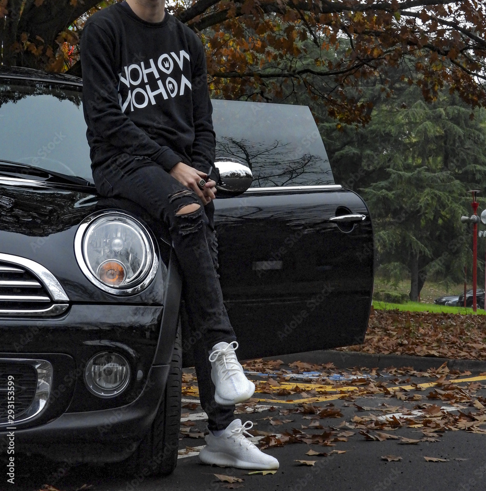 Young man wearing Adidas Yeezy 350 white shoes and sitting on a BMW Mini  car Stock Photo | Adobe Stock