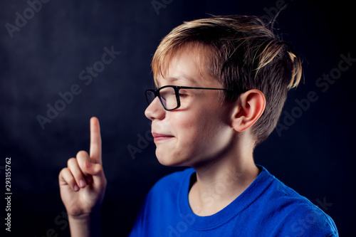 A portrait of a boy pointed finger up in front of dark background. Children and emotions concept