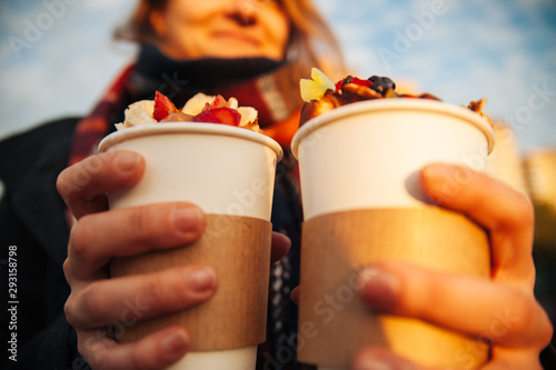 delicious Viennese waffles with fruits chocolate and syrup in a girl's hands in a paper cup, a treat for children and adults