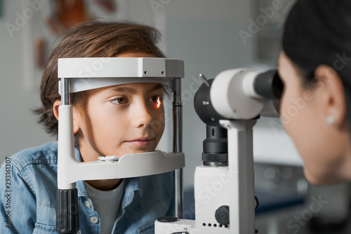 Adult female doctor ophthalmologist is checking the eye vision of cute child in modern clinic