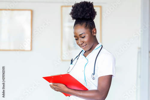 Doctor with a stethoscope, holding a notebook in her hands. Close-up of a female doctor filling up medical form at clipboard while standing straight in hospital