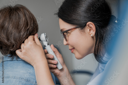 Close up of doctor examining boy's ear with otoscope in medical cabinet photo