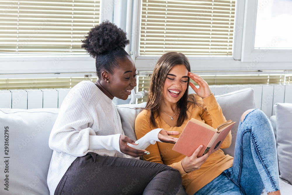 Two women laughing about funny stories from books at home. Friendship and care, happy girl friends. African American and caucasian best friends Two women laughing about funny stories from books at home. Friendship and care, happy girl friends. African American and caucasian best friends