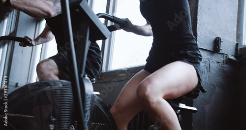 Close-up young athletic Caucasian man and woman working out on gym bike machines slow motion. Healthy lifestyle concept. photo