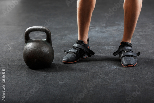 A man's feet in black sneakers with black gymnastic kettlebell