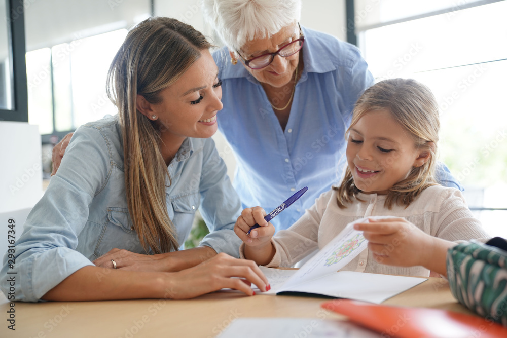 Fototapeta premium Little girl doing homework, mom and grandma watching her