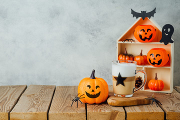 Halloween holiday concept with latte macchiato coffee cup and jack o lantern glitter pumpkin decor on wooden table