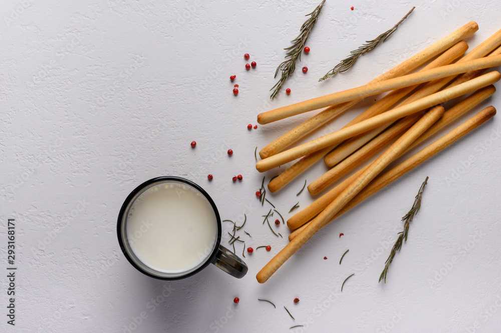 Traditional Italian breadsticks grissini lie on a light textured table. Near a mug of milk and sprigs of rosemary. Top view Traditional Italian breadsticks grissini lie on a light textured table. Near a mug of milk and sprigs of rosemary. Top view