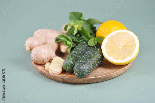 Ingredients for making a fresh, detox sassi drink. Lemon, cucumbers, ginger root, mint on a round wooden tray. Light background. Close-up.