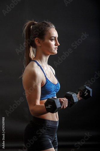 A young sport lady with ponytail in fitness clothes training with dumbells