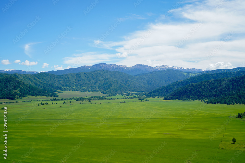 Landscape with mountains and green grass field, blue sky with clouds
