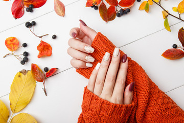 Autumn manicure. Beautyful nails design with autumn leaves. Top view. cozy autumn image. Cozy nails design. autumn leaves. Manicured woman's hands in warm wool turquoise sweater on wooden background