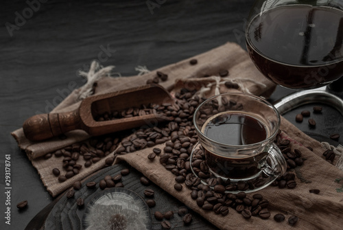 Cup of coffee and coffee beans roating with old wooden scoop and coffee beans around on the wooden and dark stone background. Oblique view from the top with copy space for your text.