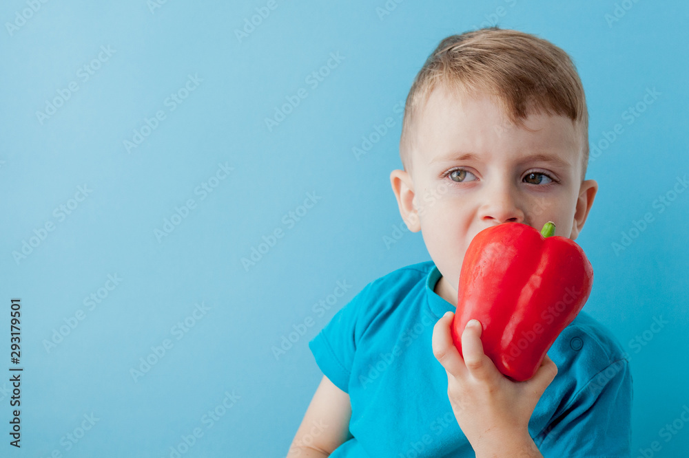 Little kid holding pepper in his hands on blue background. Vegan and healthy concept Little kid holding pepper in his hands on blue background. Vegan and healthy concept