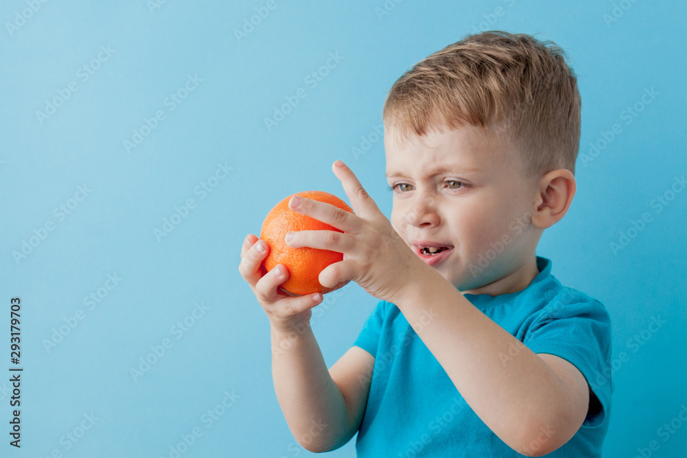 Little Boy Holding an Orange in his hands on blue background, diet and exercise for good health concept Little Boy Holding an Orange in his hands on blue background, diet and exercise for good health concept