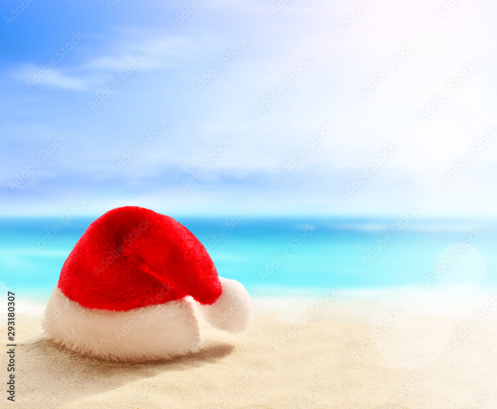 Christmas holidays concept. Santa claus hat on summer sand beach Christmas holidays concept. Santa claus hat on summer sand beach