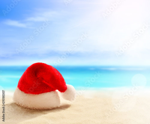 Christmas holidays concept. Santa claus hat on summer sand beach
