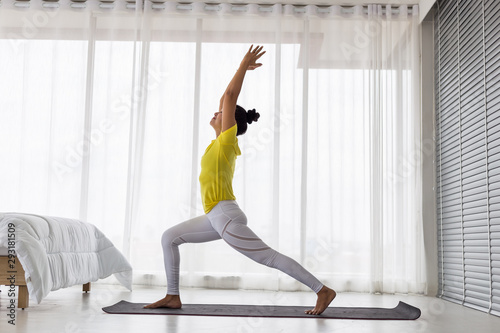 young Asian lady wearing yellow t shirt doing exercise Yoga pose in the bedroom in the morning.